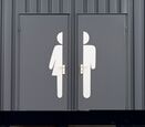 a pair of gray restroom doors, one labeled with a large pictogram of a woman and the other of a man