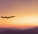 an airplane flying in the sky with purple mountains in the background at sunset