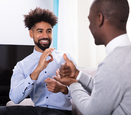a black man wearing a blue button up is signing to another black man wearing a grey cardigan
