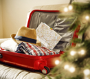 A red suitcase filled with clothing and a brightly lit Christmas tree on the right.