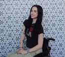 Bella Mohn smiles in her wheelchair against an abstract background.